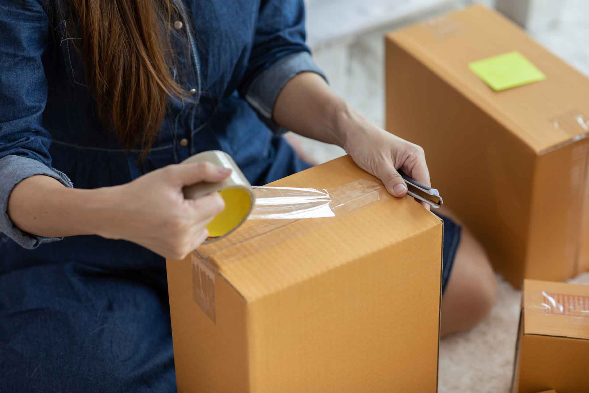 A woman taping a cardboard box shut